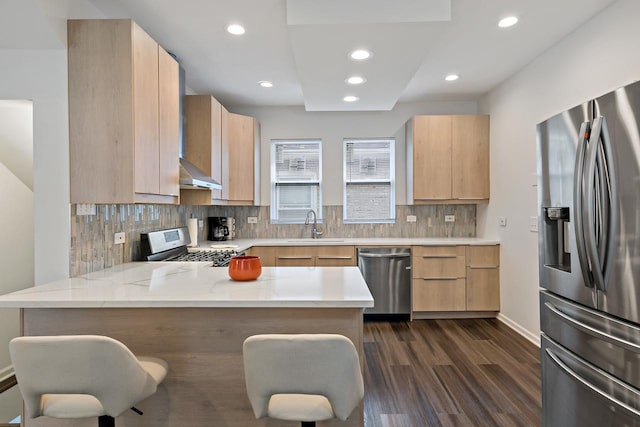 kitchen with light brown cabinetry, stainless steel appliances, kitchen peninsula, and a kitchen bar