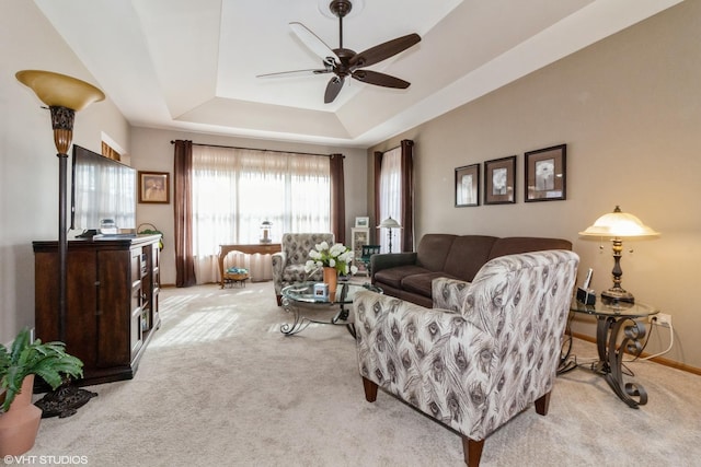 carpeted living room with a raised ceiling and ceiling fan