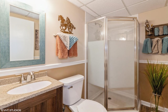 bathroom with vanity, a shower with door, toilet, and a drop ceiling