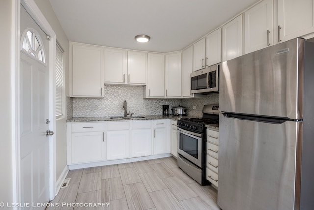 kitchen with sink, white cabinetry, backsplash, stainless steel appliances, and stone countertops