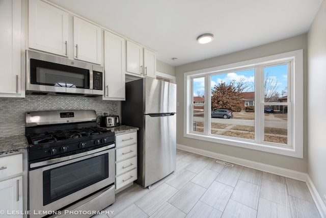 kitchen with tasteful backsplash, white cabinetry, appliances with stainless steel finishes, and dark stone counters