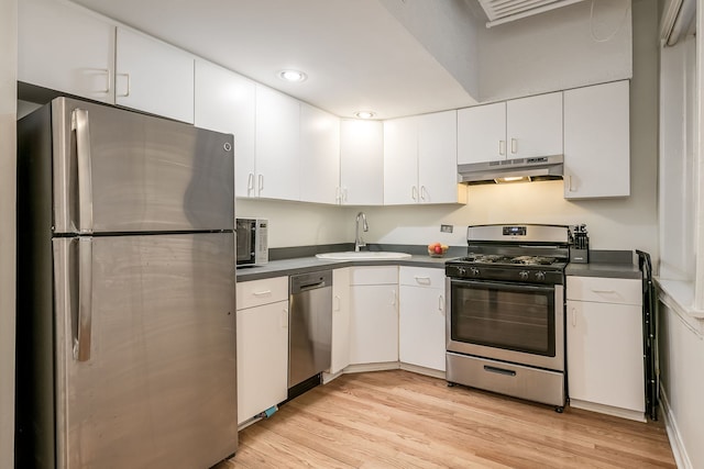 kitchen featuring appliances with stainless steel finishes, dark countertops, a sink, and under cabinet range hood