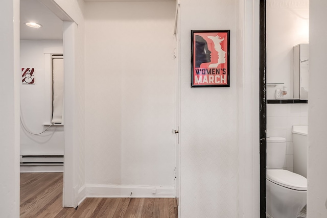 hallway featuring a baseboard radiator, wood finished floors, and tile walls