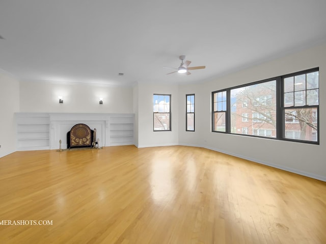 unfurnished living room featuring built in features, baseboards, a fireplace with flush hearth, ceiling fan, and light wood-style floors