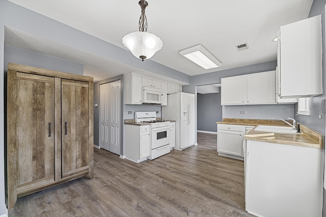 kitchen with white cabinetry, sink, hanging light fixtures, dark wood-type flooring, and white appliances