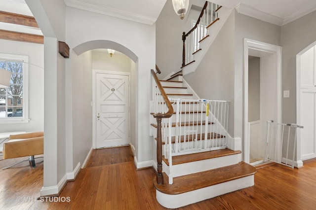 entryway featuring arched walkways, wood finished floors, baseboards, and ornamental molding