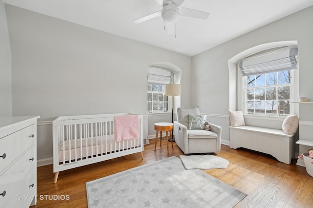 bedroom featuring baseboards, multiple windows, a nursery area, and wood finished floors