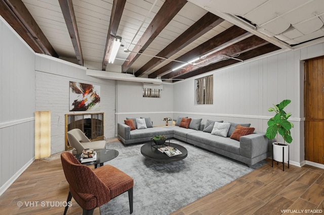 living area with beamed ceiling, a brick fireplace, and wood finished floors