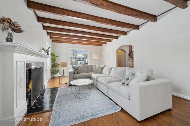 living room with beam ceiling, wood finished floors, arched walkways, and a premium fireplace