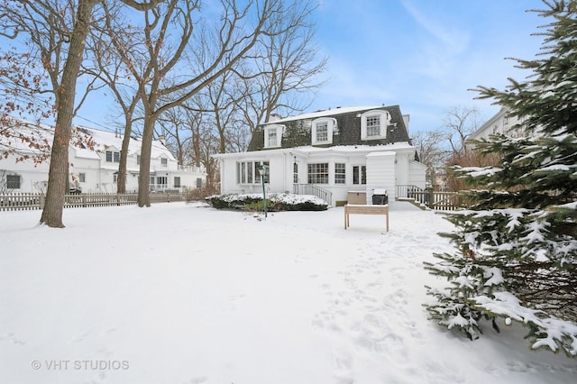 snow covered back of property featuring mansard roof and fence