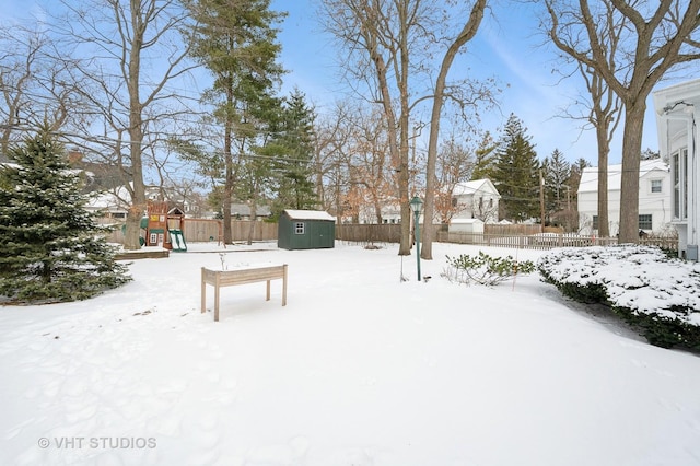 snowy yard with a fenced backyard, a storage shed, a playground, and an outdoor structure