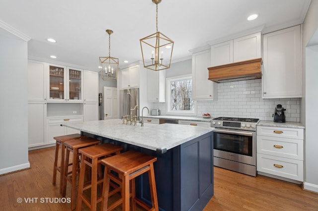 kitchen with an island with sink, white cabinets, appliances with stainless steel finishes, crown molding, and light wood-type flooring