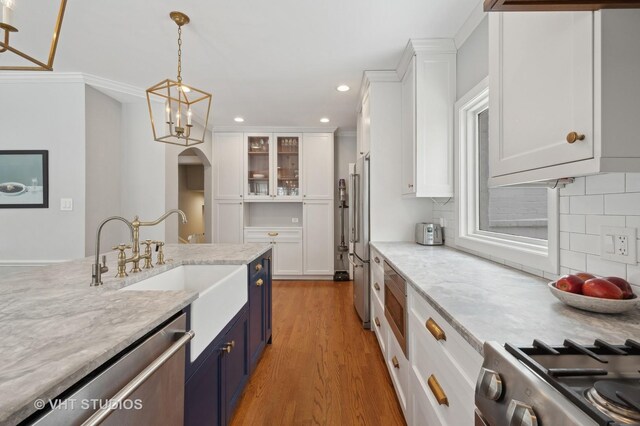 kitchen with light wood-style flooring, appliances with stainless steel finishes, arched walkways, white cabinetry, and blue cabinets