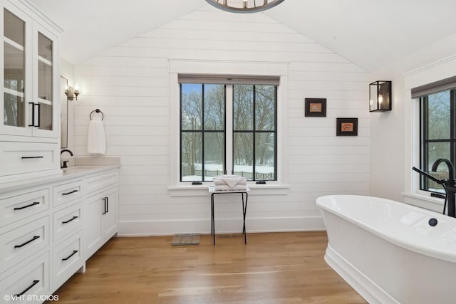 bathroom with hardwood / wood-style floors, vanity, lofted ceiling, and a bath