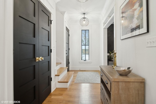 doorway to outside with ornamental molding, a chandelier, and light wood-type flooring