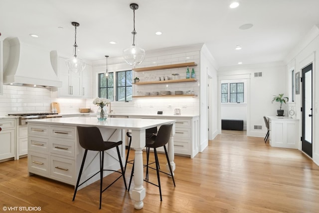 kitchen with a kitchen island, custom range hood, white cabinets, and a breakfast bar