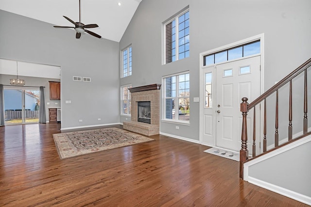 foyer featuring dark hardwood / wood-style flooring, ceiling fan with notable chandelier, a brick fireplace, and a high ceiling