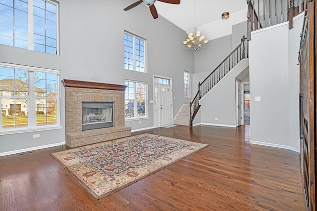 living room featuring a fireplace, dark hardwood / wood-style floors, ceiling fan with notable chandelier, and a high ceiling