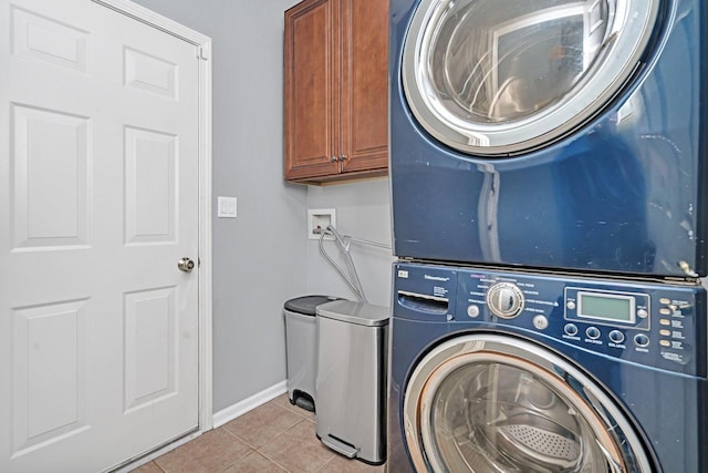 laundry area featuring stacked washer and clothes dryer, cabinets, and light tile patterned flooring