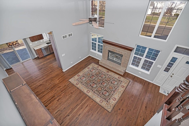 living room with a high ceiling, ceiling fan, dark hardwood / wood-style floors, and a fireplace