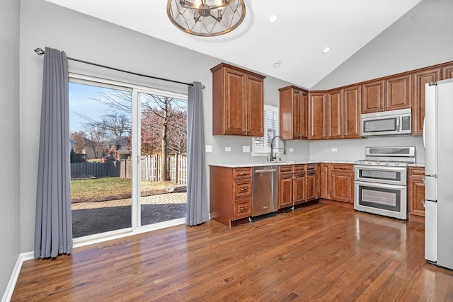 kitchen with sink, dark wood-type flooring, stainless steel appliances, light stone countertops, and vaulted ceiling