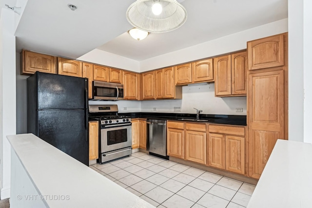 kitchen with a sink, dark countertops, appliances with stainless steel finishes, and light tile patterned flooring