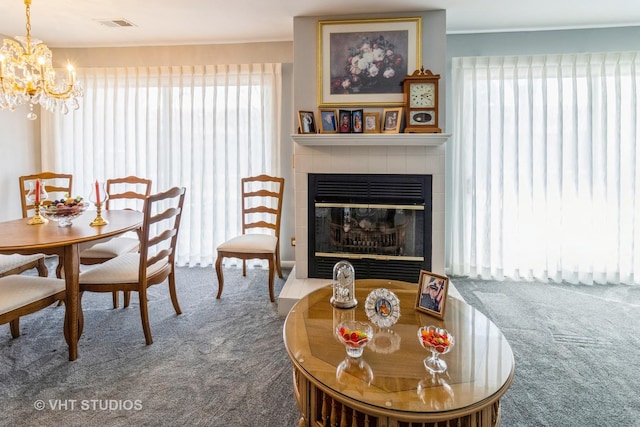 dining area featuring a tiled fireplace, ornamental molding, carpet floors, and an inviting chandelier