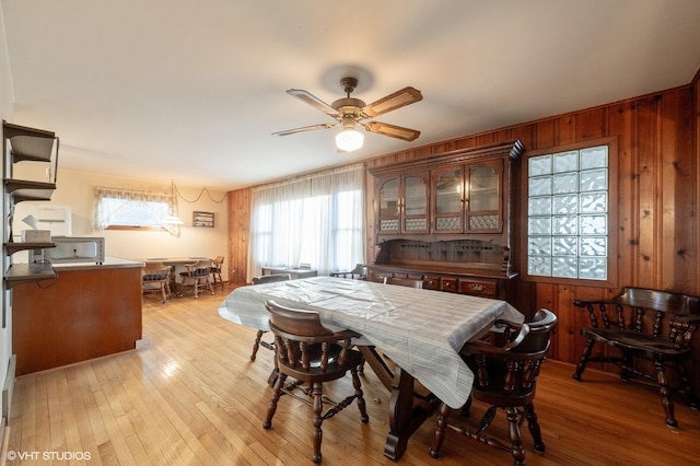 dining space with ceiling fan, wooden walls, and light wood-type flooring