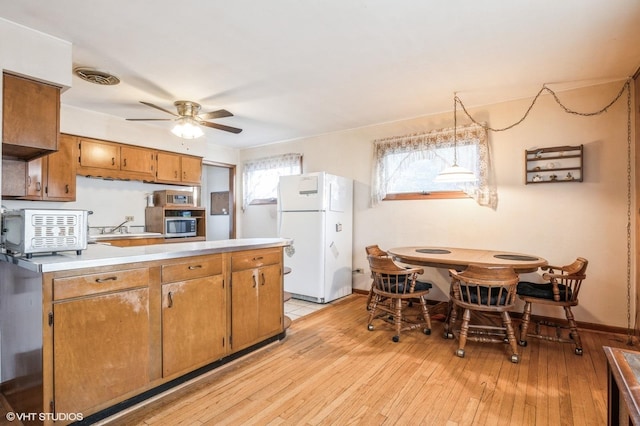 kitchen featuring sink, ceiling fan, white fridge, decorative light fixtures, and light wood-type flooring