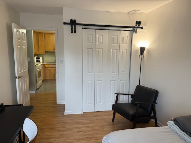 bedroom with a barn door, light wood-type flooring, and a closet