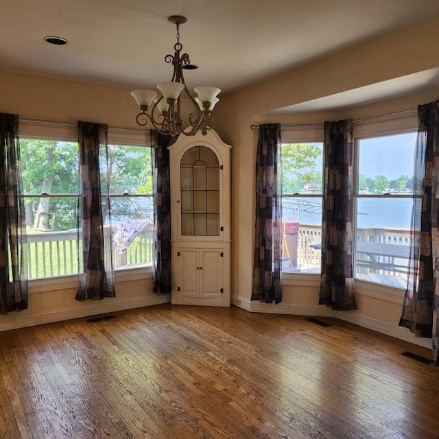 unfurnished dining area featuring a water view, hardwood / wood-style floors, and an inviting chandelier