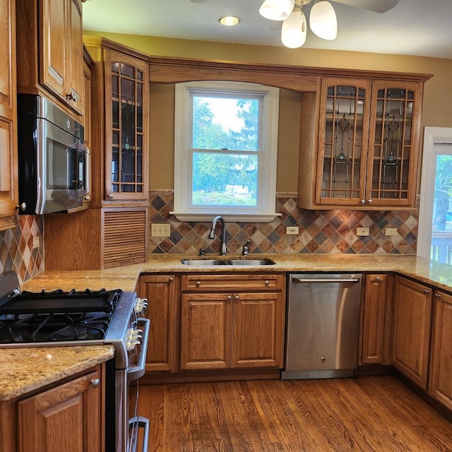 kitchen with sink, dark wood-type flooring, backsplash, stainless steel appliances, and light stone countertops