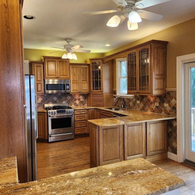 kitchen with sink, light wood-type flooring, appliances with stainless steel finishes, kitchen peninsula, and ceiling fan