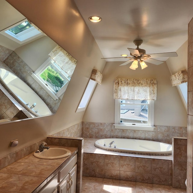 bathroom featuring a relaxing tiled tub, ceiling fan, vanity, and a skylight