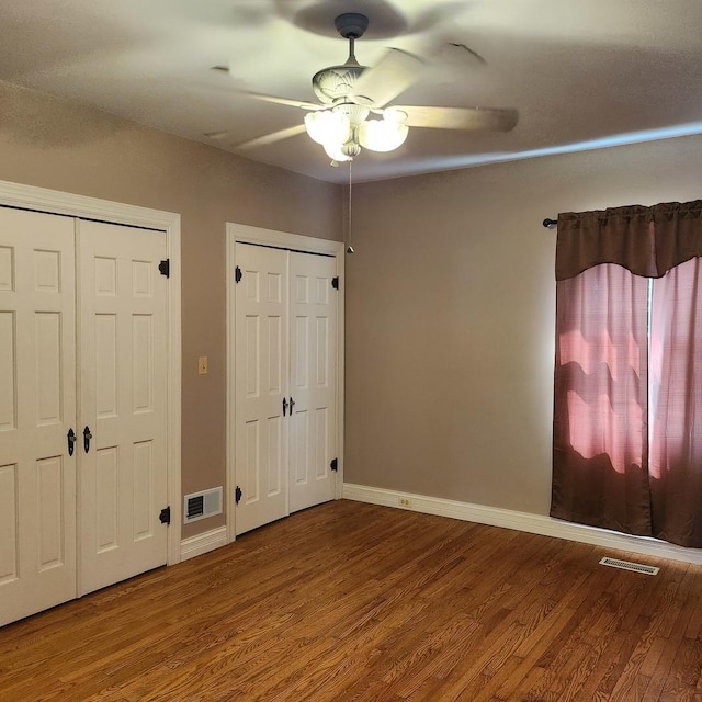 unfurnished bedroom with two closets, ceiling fan, and hardwood / wood-style flooring