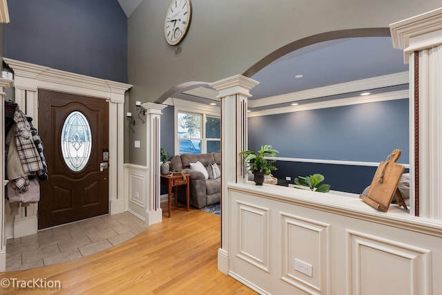 entrance foyer with arched walkways, crown molding, decorative columns, wainscoting, and light wood-type flooring