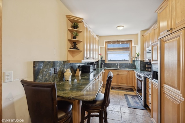 kitchen featuring a kitchen bar, light brown cabinetry, sink, dark stone counters, and stainless steel appliances