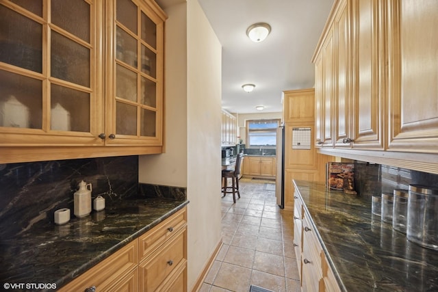 kitchen with sink, dark stone countertops, light tile patterned floors, and decorative backsplash