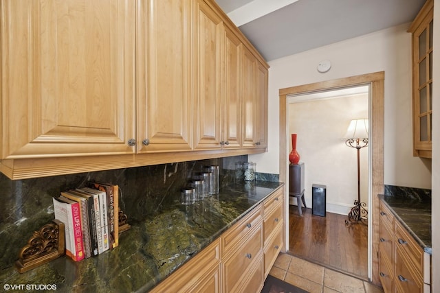 kitchen with dark stone countertops, decorative backsplash, dark tile patterned floors, and light brown cabinets