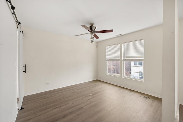 spare room featuring hardwood / wood-style flooring, a barn door, and ceiling fan