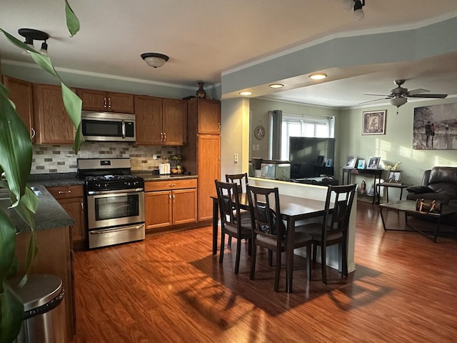 kitchen featuring tasteful backsplash, ceiling fan, stainless steel appliances, crown molding, and dark wood-type flooring