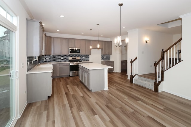 kitchen featuring gray cabinets, hanging light fixtures, backsplash, stainless steel appliances, and a kitchen island