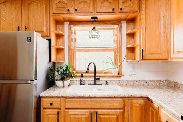 kitchen featuring stainless steel refrigerator, light stone countertops, sink, and hanging light fixtures