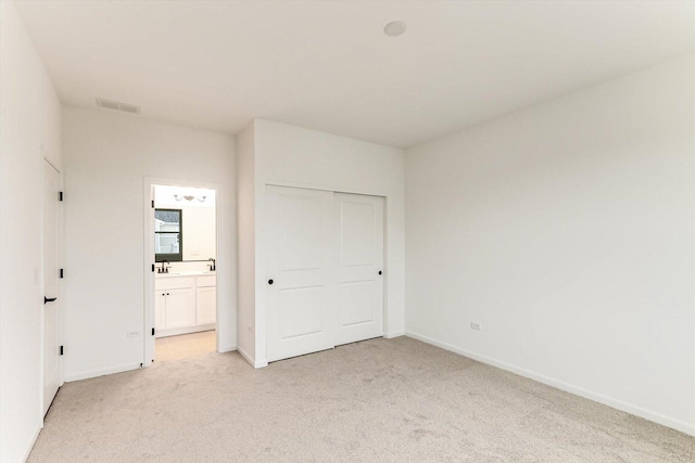 unfurnished bedroom featuring ensuite bath, a closet, and light carpet