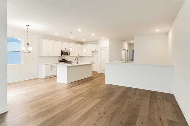 kitchen with appliances with stainless steel finishes, decorative light fixtures, white cabinetry, a center island with sink, and light hardwood / wood-style flooring