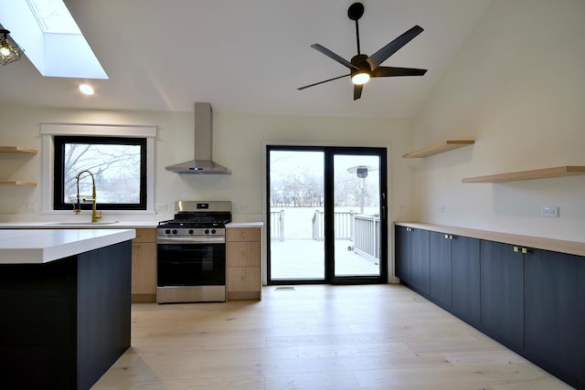 kitchen with light hardwood / wood-style floors, stainless steel gas range, sink, and wall chimney range hood