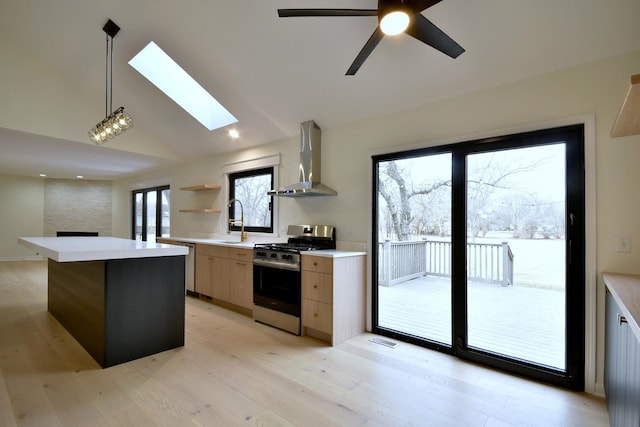 kitchen with appliances with stainless steel finishes, hanging light fixtures, a center island, wall chimney exhaust hood, and light wood-type flooring