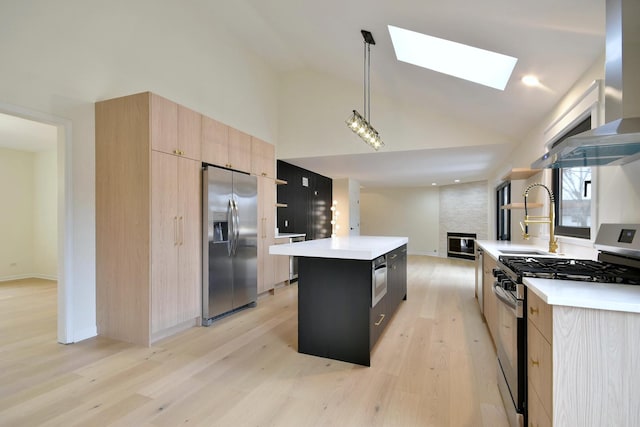 kitchen with sink, a kitchen island with sink, hanging light fixtures, stainless steel appliances, and wall chimney exhaust hood