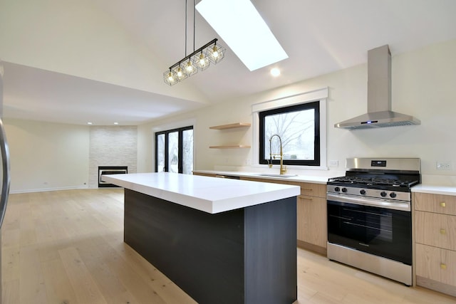 kitchen featuring sink, hanging light fixtures, a center island, gas range, and wall chimney exhaust hood