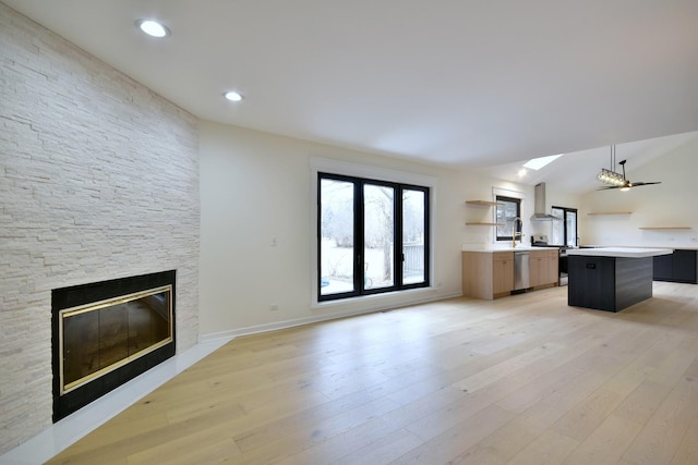 unfurnished living room with a stone fireplace, lofted ceiling, ceiling fan, and light hardwood / wood-style flooring